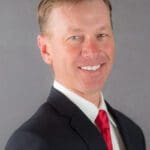 Headshot of a smiling man in a suit and red tie.