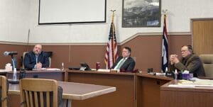 Three men sit at a conference table.