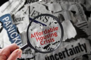 Magnifying glass over newspaper headlines about affordable housing crisis.